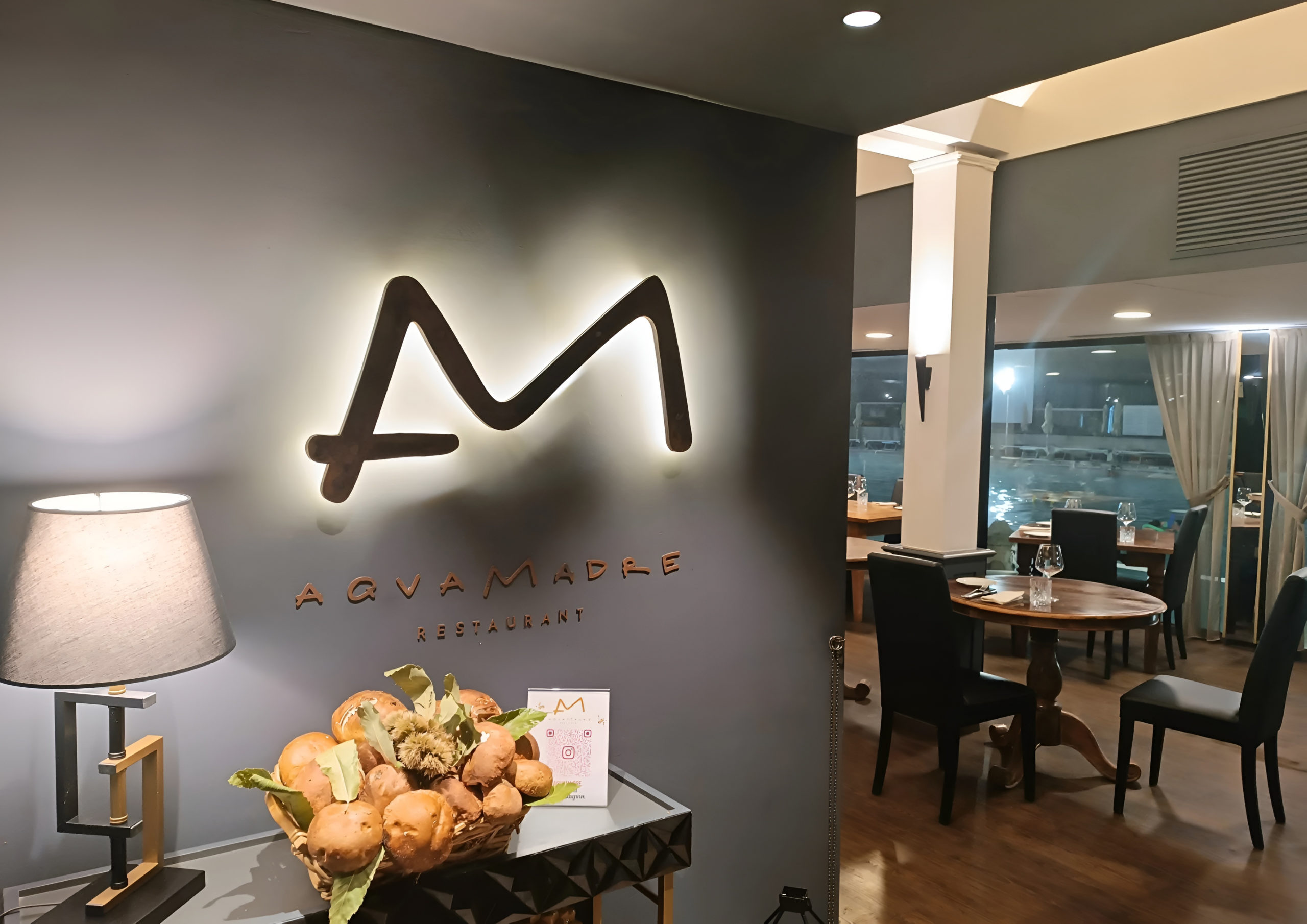 L’ingresso del ristorante Aqvamadre, con il logo illuminato e la sala apparecchiata